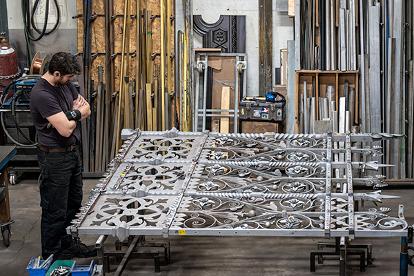 A heritage metal restoration professional inspects part of the main Queen&rsquo;s Gates at Dominion Restoration&rsquo;s Montr&eacute;al workshop.