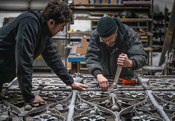 Two heritage metal restoration professionals reassemble a gate in Dominion Restoration&rsquo;s workshop.